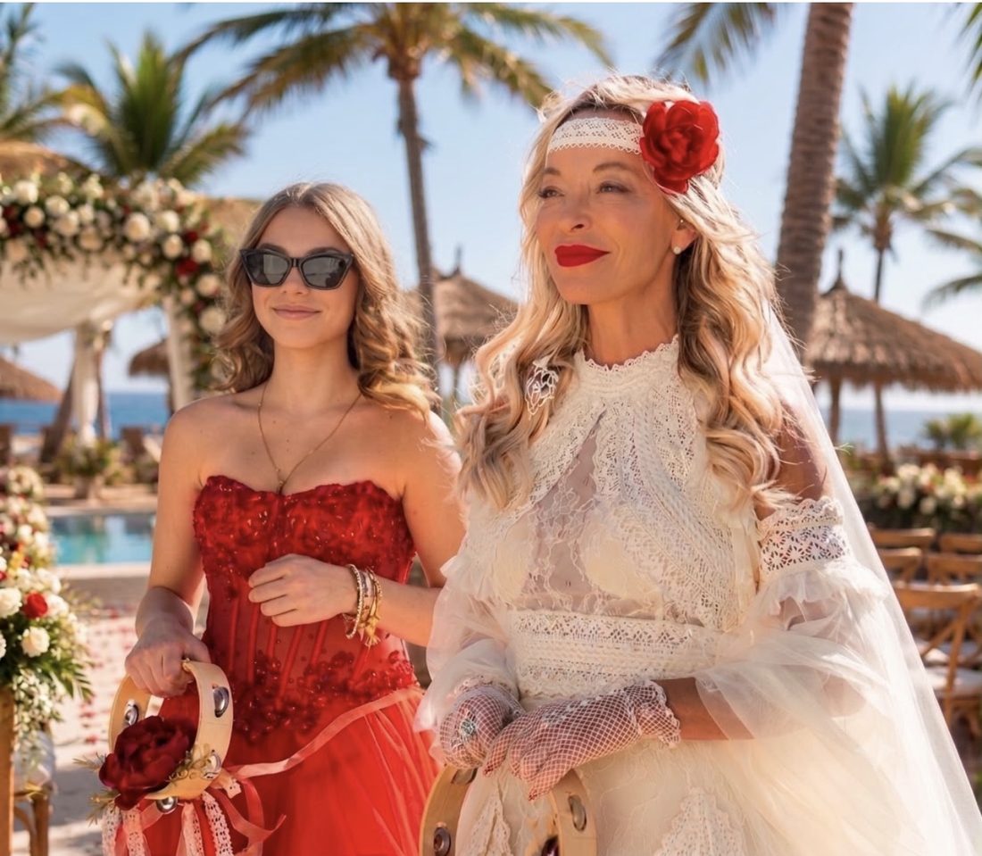 Novia con una rosa roja en el pelo junto a una invitada vestida de rojo