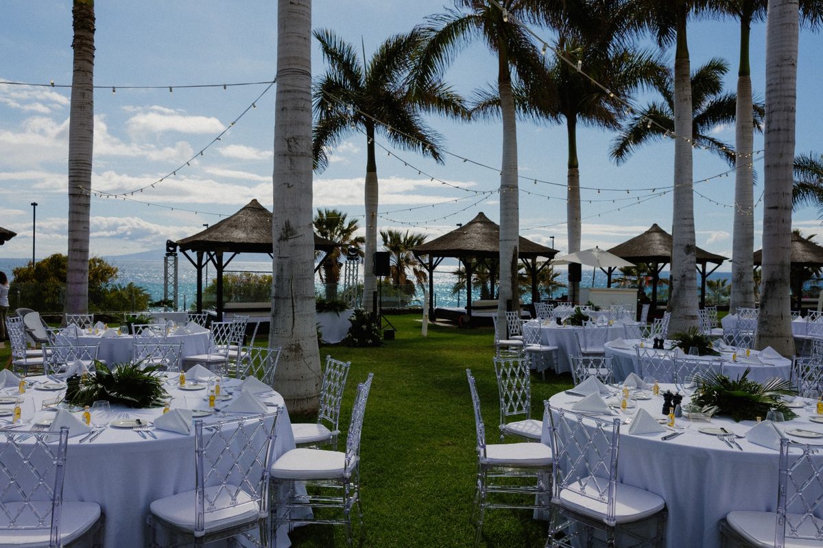 Mesas del banquete con mantelería blanca bajo palmeras y guirnaldas de luces