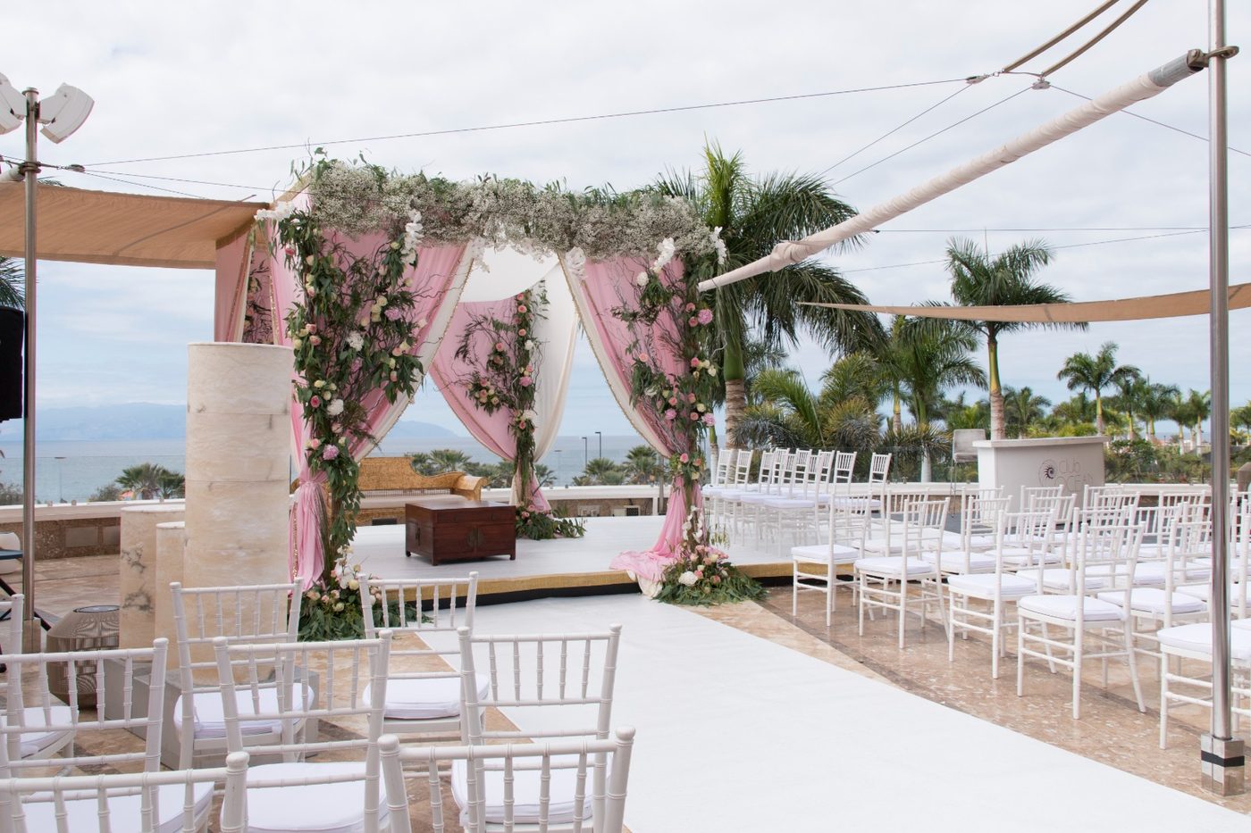 Montaje de ceremonia con arco floral y sillas blancas en una terraza con vistas al mar